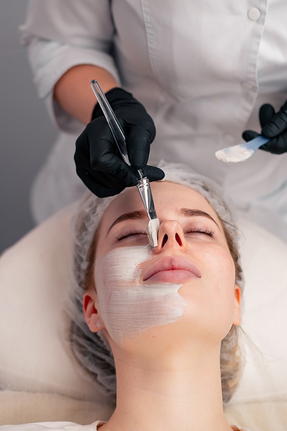 close-up beautician in gloves applies a mask on the face of a client with a brush care for skin